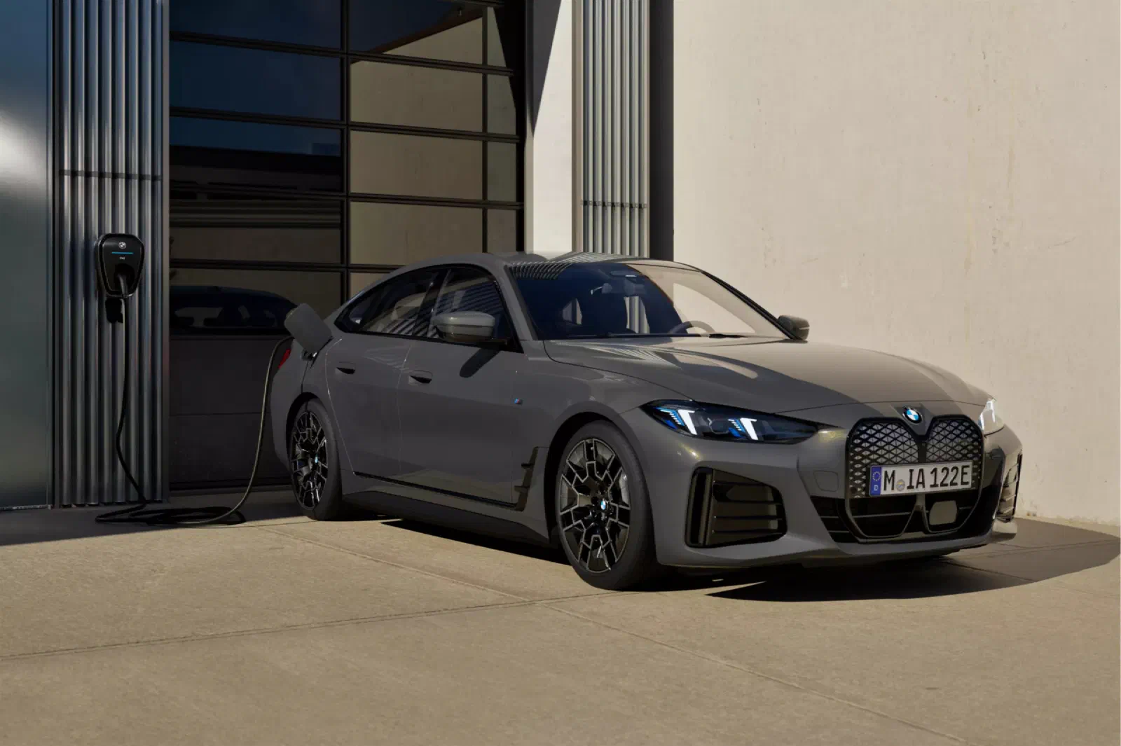 Grijze BMW i4 schuin van voren voor een gebouw, aangesloten op een wallbox aan de muur.