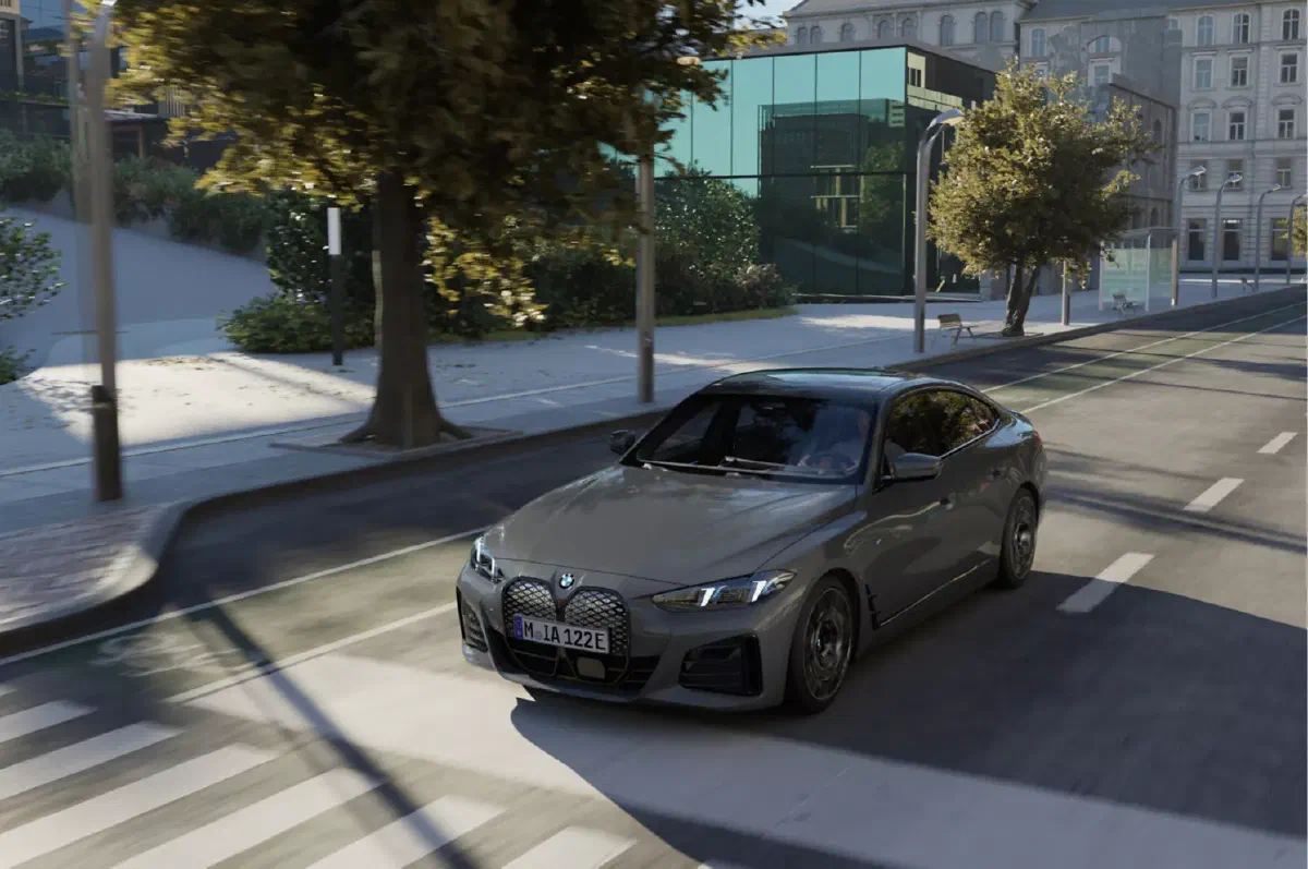 Grijze BMW i4 rijdend door een stadsstraat met bomen en glazen gebouwen.